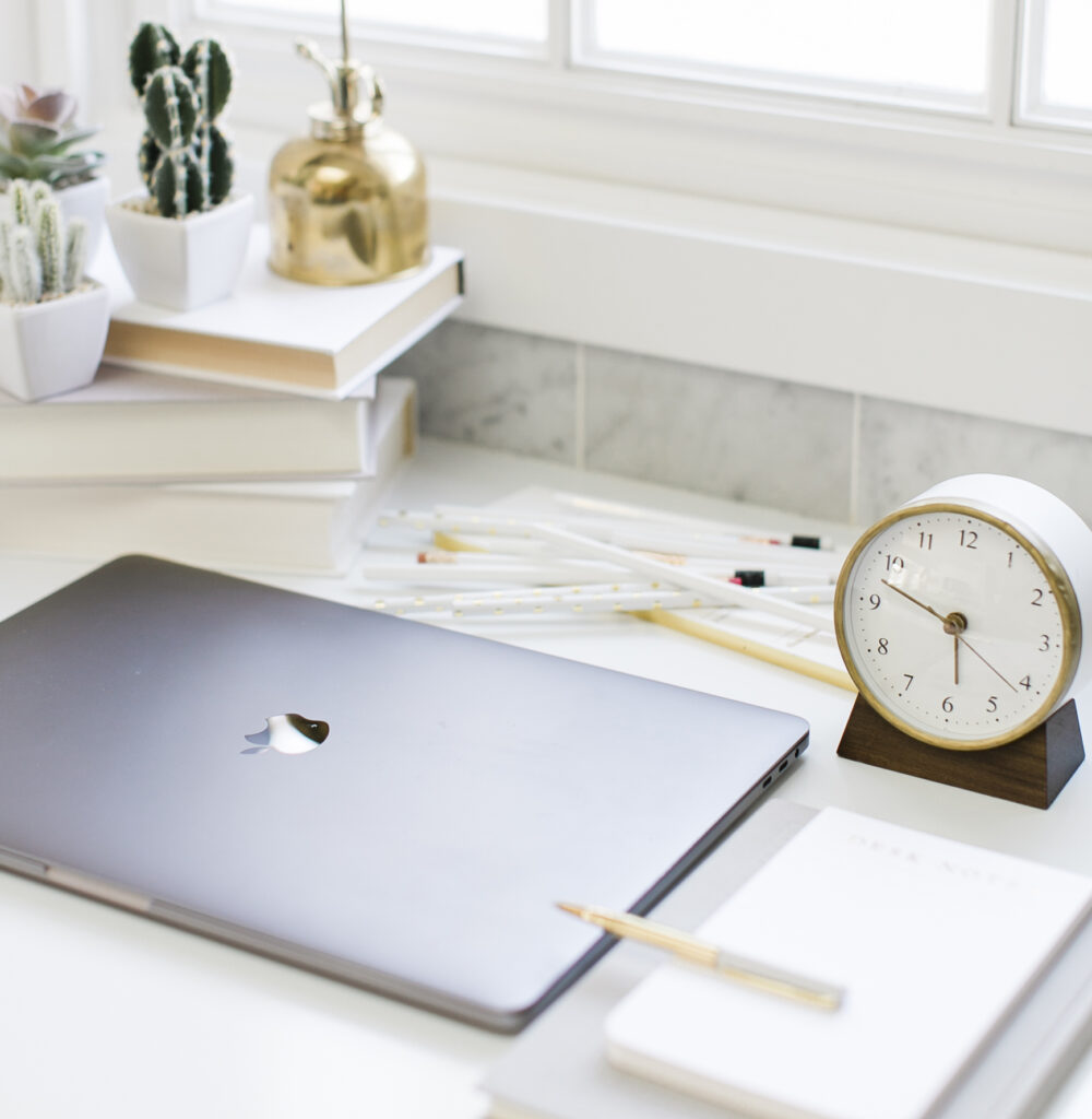 laptop, paper pad, pencils, and clock on a table